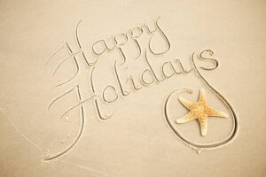 Happy Holidays message in calligraphy script handwritten in smooth brown sand with a starfish flourish